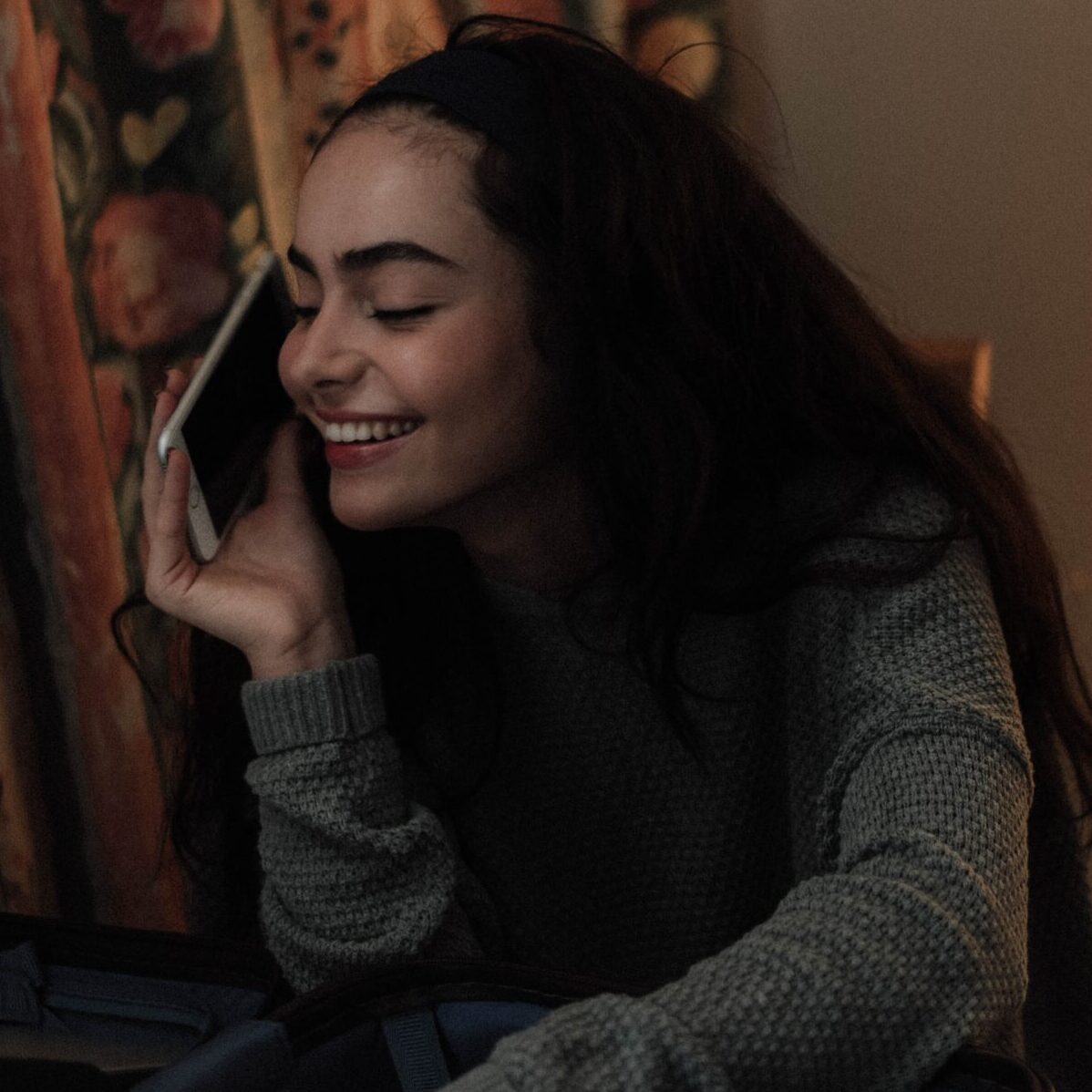 Person with long curly hair smiling while talking on the phone.