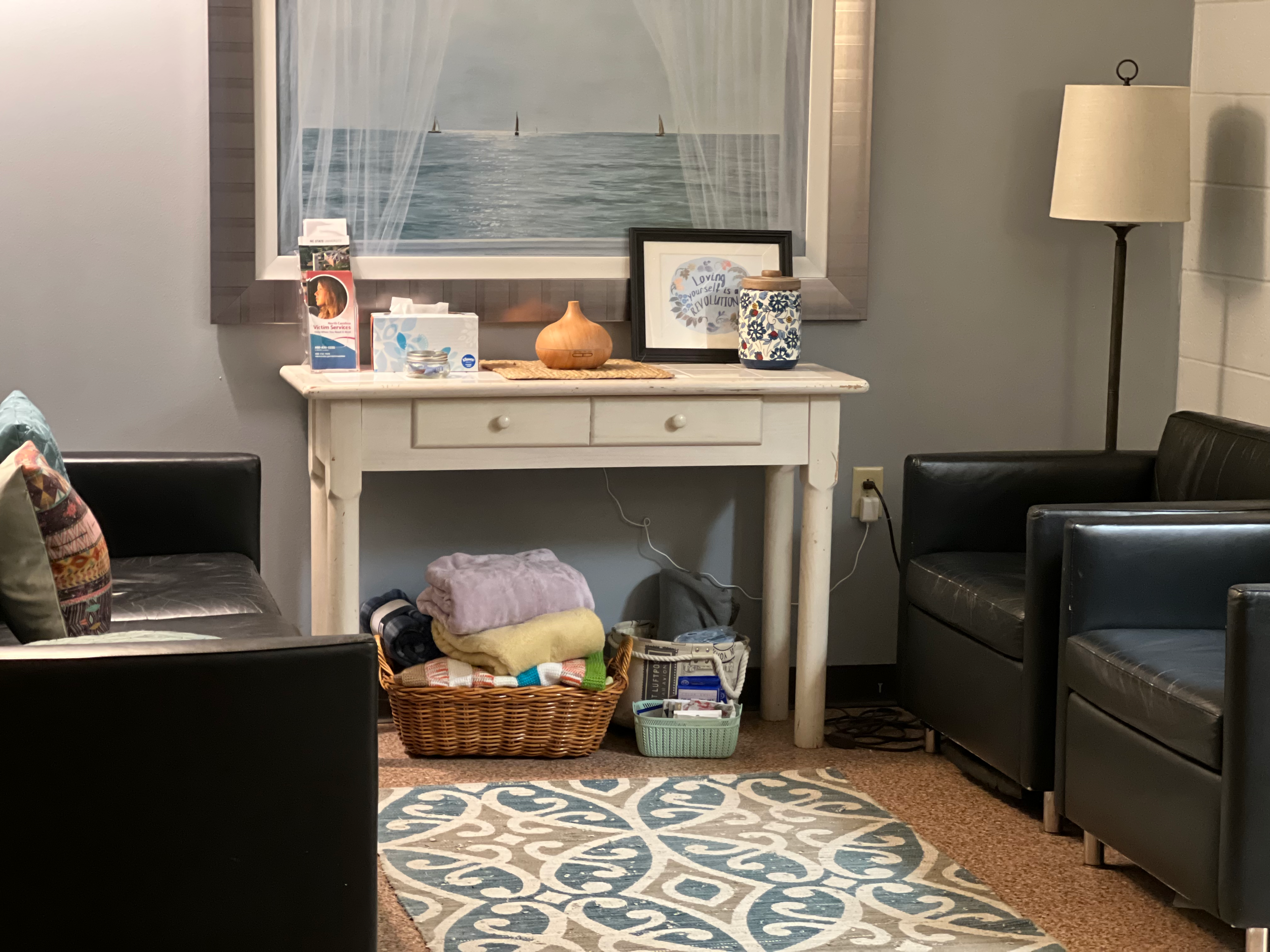 Solace Center seating area. InterAct Solace Center room with holistic attention to comfort and care. The photo shows calming, neutral colors, soothing items such as blankets, adaptive lighting, comfortable seating, rugs to walk on, and soothing wooden flooring.