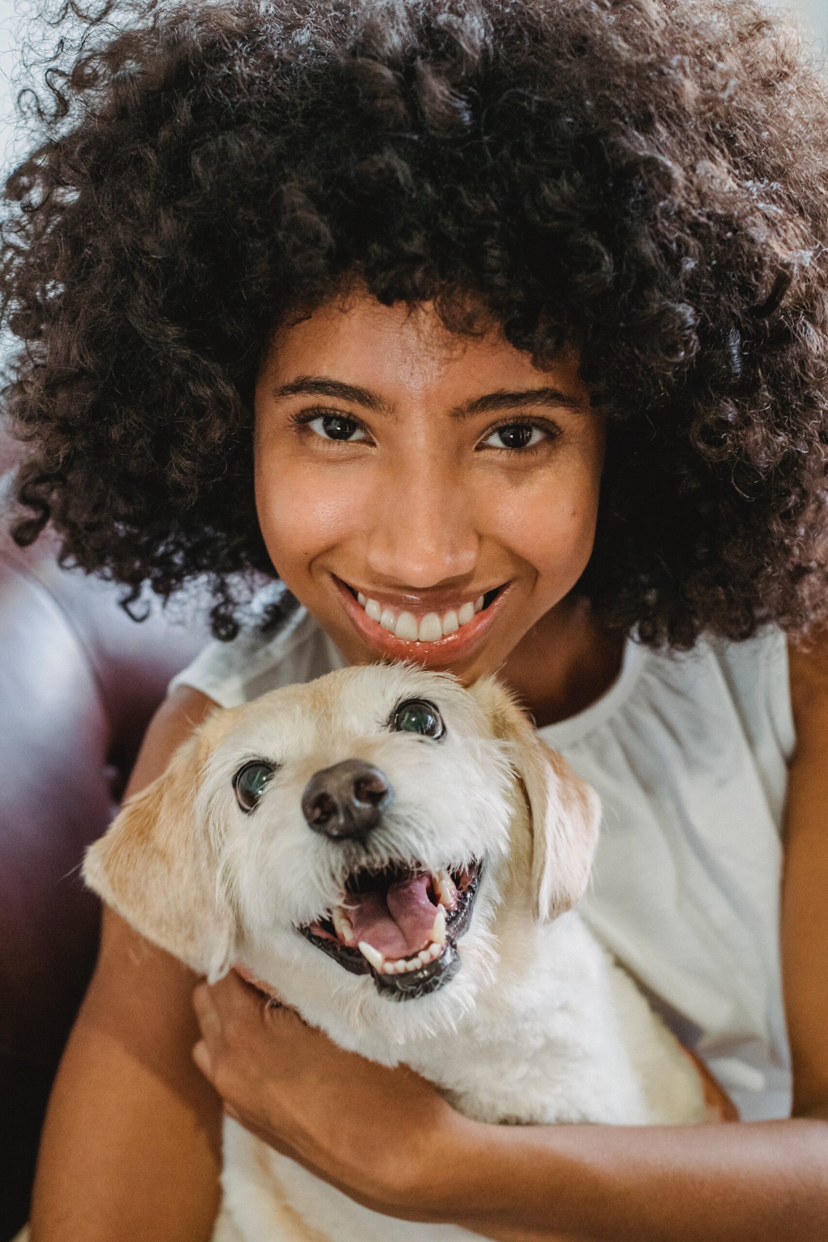 Person with curly hair holding a smiling dog with cream colored hair.